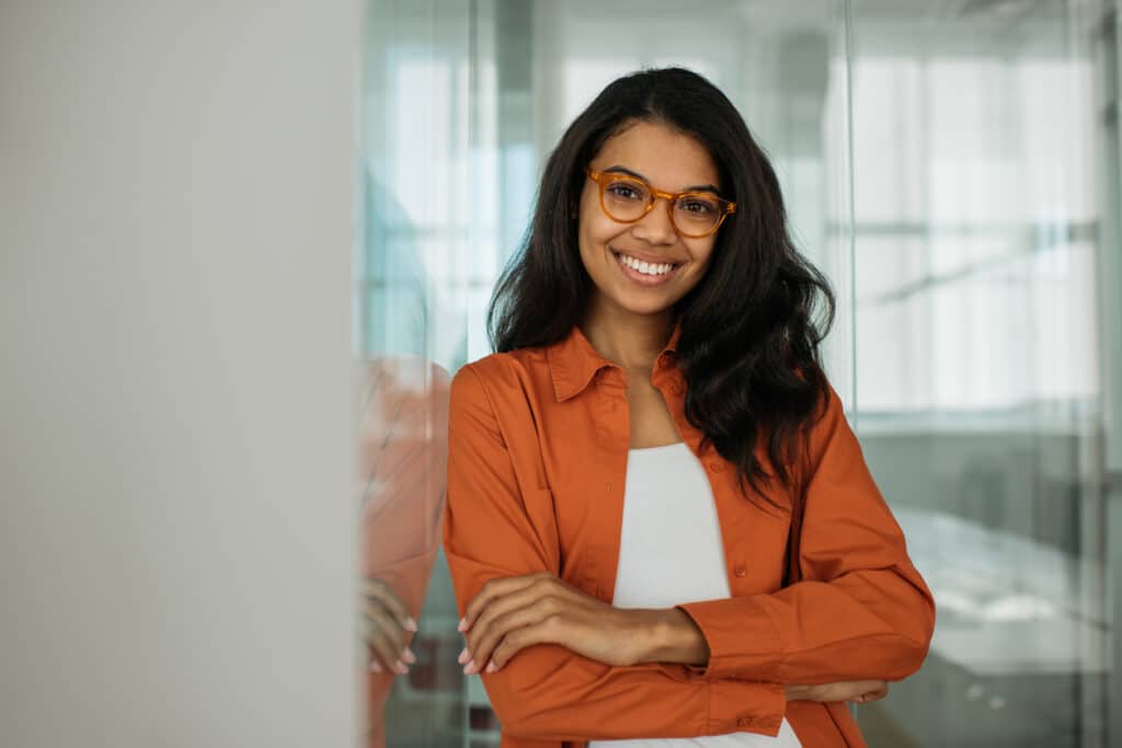 Smiling African American business woman wearing stylish eyeglasses looking at camera standing in modern office. Successful business and career concept